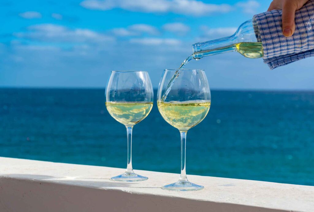 two glasses of white wine with the ocean as a background