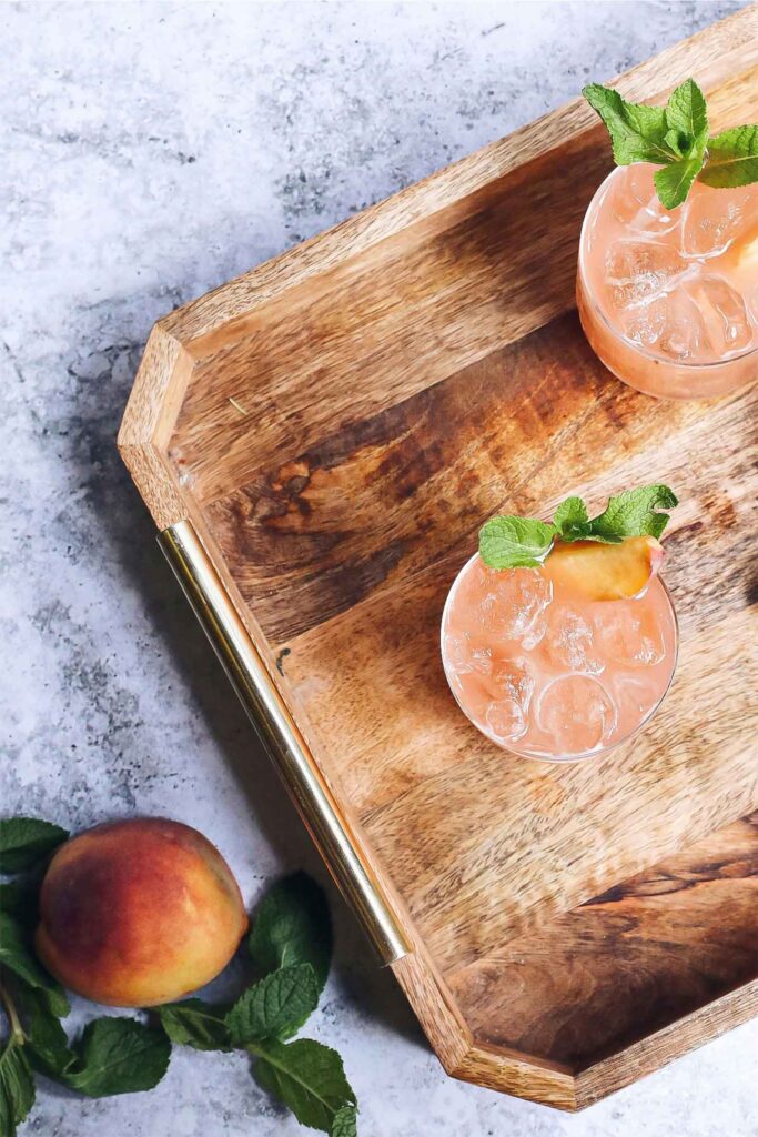 peach vodka cocktails on a cutting board with a single peach on the side