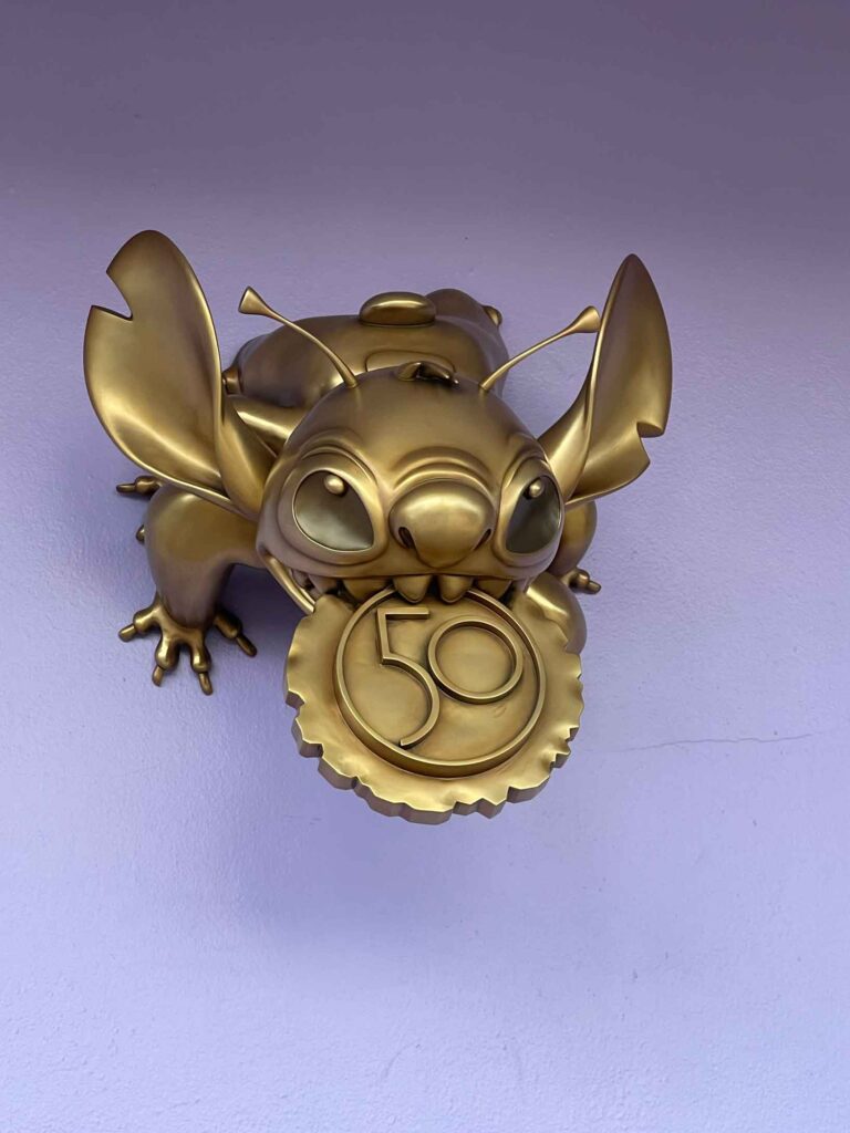 Stitch gold statue for 50th anniversary on purple wall in tomorrowland