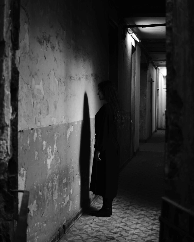 black and white photo of a hallway and a dark figure standing towards the wall - looking at the wall